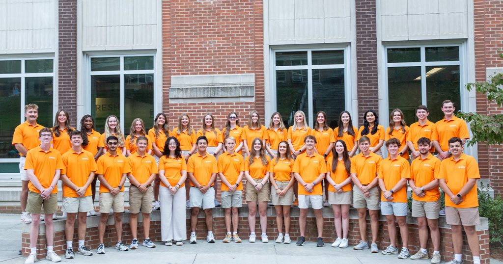 2024 2025 Tickle College of Engineering Ambassadors wearing orange standing in 2 lines in front of Zeanah Engineering Complex